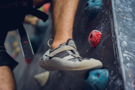 A strong male climber climbs an artificial wall with colorful grips and ropes.