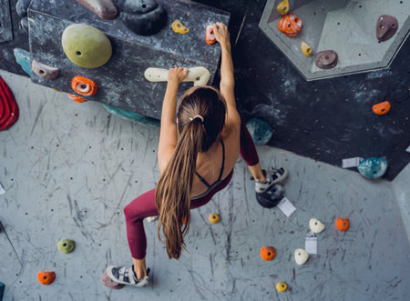 A strong female climber climbs an artificial wall with colorful grips and ropes.の写真素材