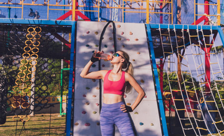 Athletic young woman drinking water after working out and climbing at the artificial rock in...
