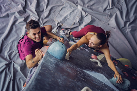A strong couple of climbers climb an artificial wall with colorful grips and ropes.の写真素材