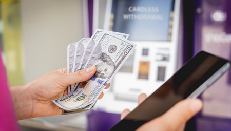 Young woman using the smart phone for cardless withdrawing the cash near the ATMの写真素材