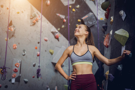 A strong female climber climbs an artificial wall with colorful grips and ropes.の写真素材