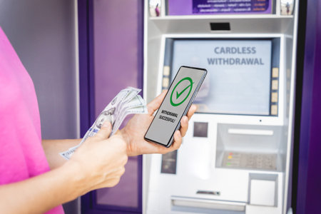 Young woman using the smart phone for cardless withdrawing the cash near the ATM