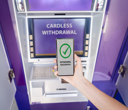 Young woman using the smart phone for cardless withdrawing the cash near the ATMの写真素材