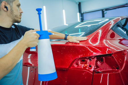 Worker in car service sprays water on the car before applying an protective film.の写真素材