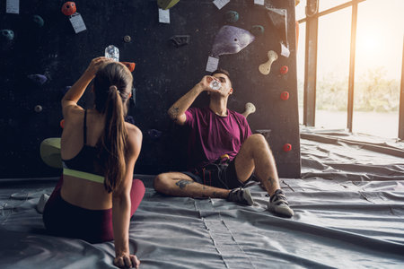 A strong couple of climbers relax near artificial wall with colorful grips and ropes.の写真素材