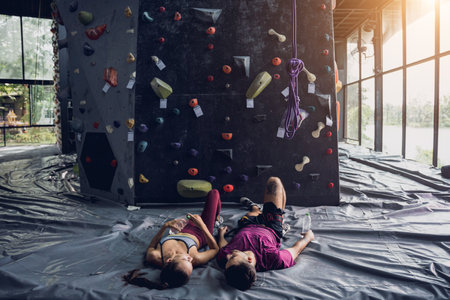 A strong couple of climbers relax near artificial wall with colorful grips and ropes.の写真素材