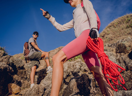 Young couple climbs with a rope to the top in the mountains near the ocean