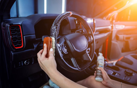 Young woman cleaning the steering wheel of car using a special brush with foamの写真素材