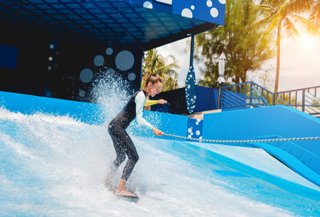 Beautiful young woman surfing on a wave simulator at a water amusement park
