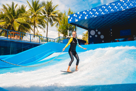 Beautiful young woman surfing with trainer on a wave simulator at a water amusement park