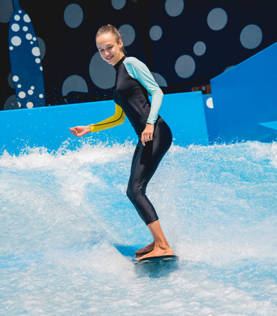 Beautiful young woman surfing on a wave simulator at a water amusement park