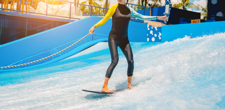 Beautiful young woman surfing on a wave simulator at a water amusement park