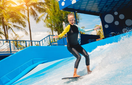 Beautiful young woman surfing on a wave simulator at a water amusement park