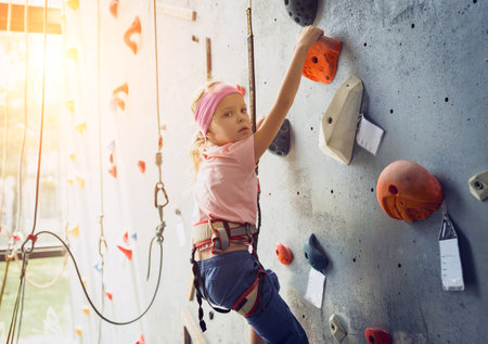A strong baby climber climbs an artificial wall with colorful grips and ropes.の写真素材