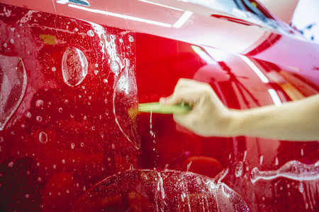 The process of installing protective film on the new red car.