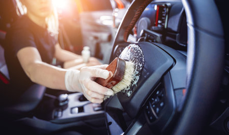 Young woman cleaning the steering wheel of car using a special brush with foam