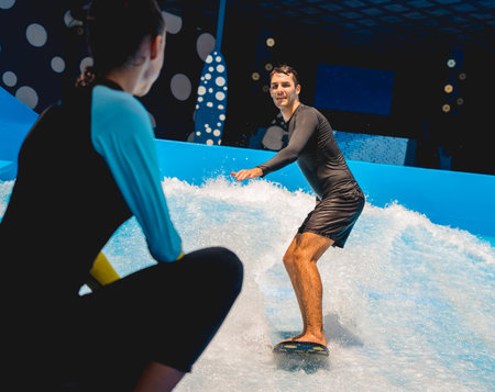 Young man surfing with trainer on a wave simulator at a water amusement parkの写真素材