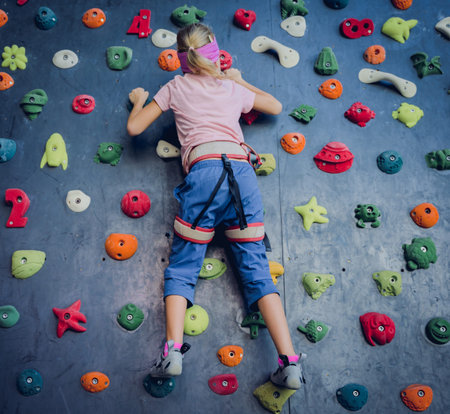 A strong baby climber climbs an artificial wall with colorful grips and ropes.