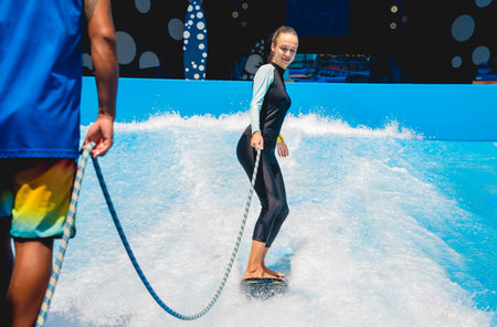 Beautiful young woman surfing with trainer on a wave simulator at a water amusement park