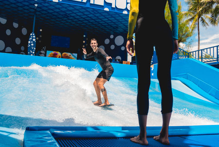 Young man surfing with trainer on a wave simulator at a water amusement parkの写真素材