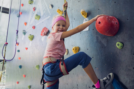 A strong baby climber climbs an artificial wall with colorful grips and ropes.の写真素材
