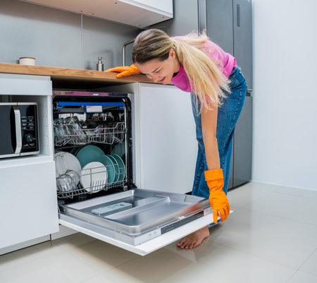 Young woman takes dishes out of the dishwasher machineの写真素材