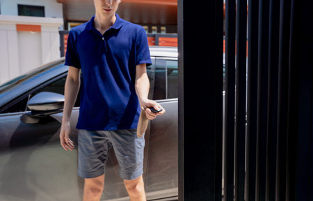 Young man using remote control to open automatic sliding front gate at modern villa