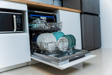 The white kitchen and opened dishwasher with clean dishes