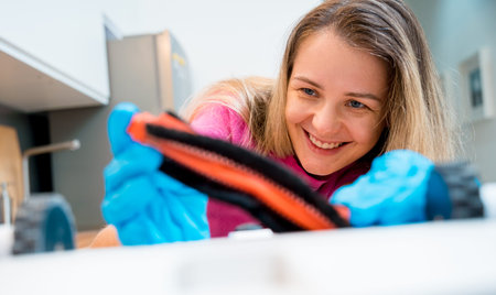 A young woman cleans a robot vacuum cleaner from dirt after cleaning.
