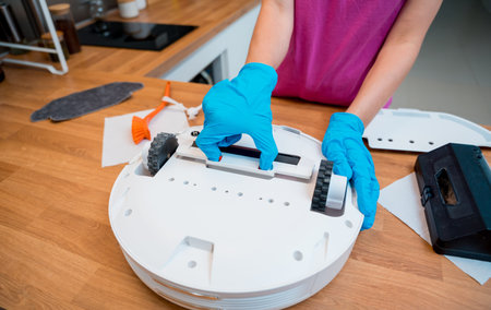 A young woman cleans a robot vacuum cleaner from dirt after cleaning.