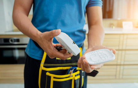 A technician installs a security alarm siren in a modern apartment.