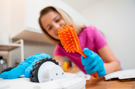 A young woman cleans a robot vacuum cleaner from dirt after cleaning.の写真素材