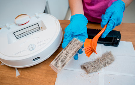 A young woman cleans a robot vacuum cleaner from dirt after cleaning.の写真素材