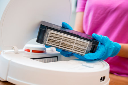 A young woman cleans a robot vacuum cleaner from dirt after cleaning.の写真素材