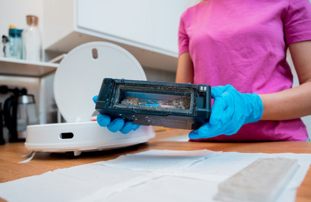 A young woman cleans a robot vacuum cleaner from dirt after cleaning.の写真素材