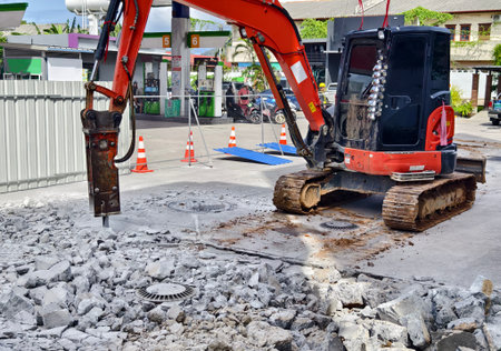 Excavator using hydraulic hammer for breaking concrete at a construction site