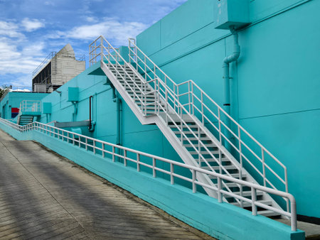 Metal stairs to blue building against sky and clouds