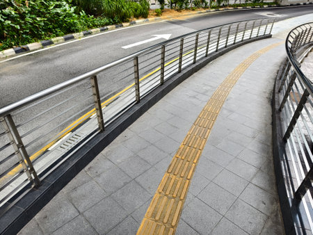 Curved path with guardrail and yellow line for blind people along the roadの写真素材