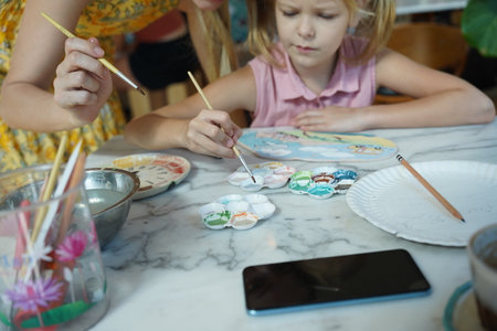 A young mother and her daughter enjoy a creative art session at homeの写真素材