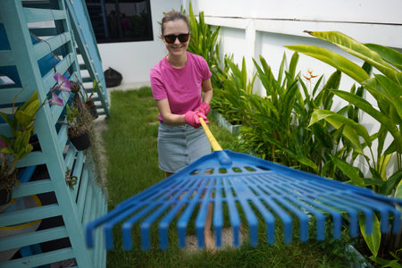 A woman raking the lawn at the backyard of her houseの写真素材