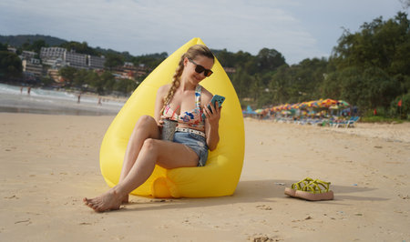 A young woman on the beach lounging on a yellow bean bagの写真素材