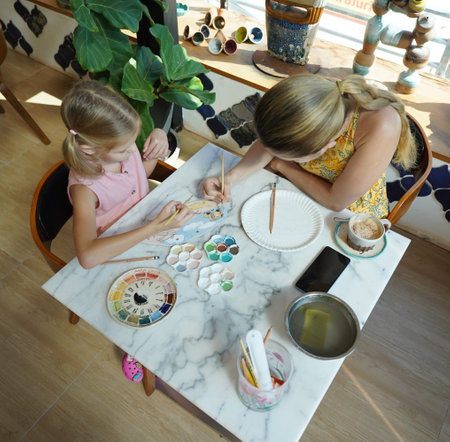 A young mother and her daughter enjoy a creative art session at homeの写真素材