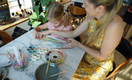 A young mother and her daughter enjoy a creative art session at homeの写真素材