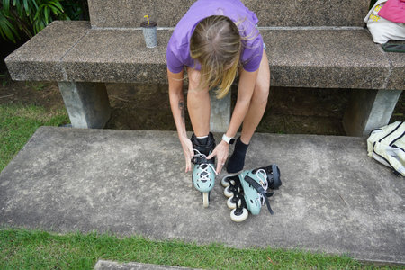 A woman is sitting on a bench and putting on her roller skatesの写真素材