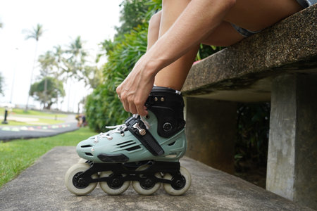 A woman is sitting on a bench and putting on her roller skates