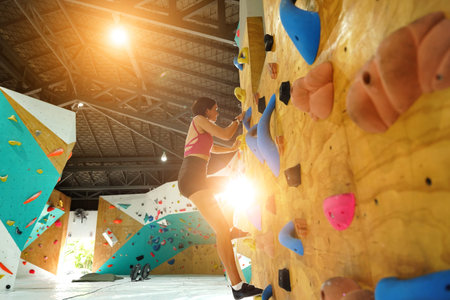 A strong female climber climbs an artificial wall with colorful grips