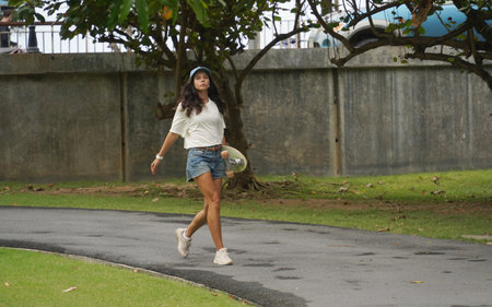 A woman is walking at the city park while carrying a skateboard in her handsの写真素材