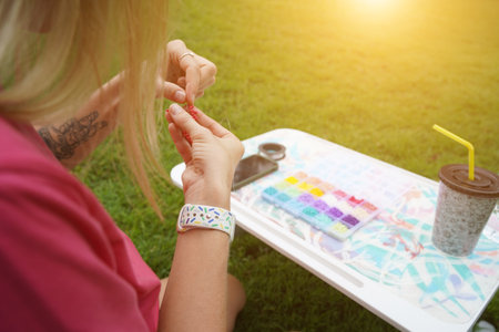 Young woman beading colorful bracelets outdoors in a parkの写真素材