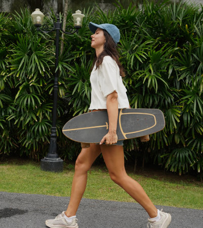 A woman is walking at the city park while carrying a skateboard in her handsの写真素材